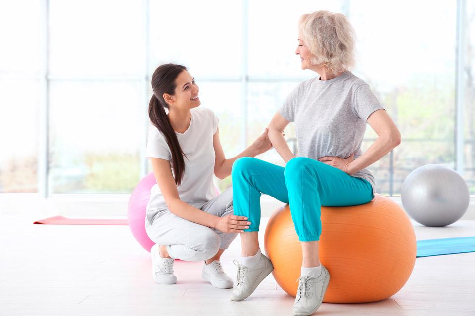 A nurse shows an elderly lady how to do exercises on the ball